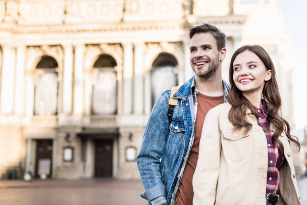Happy boyfriend and girlfriend looking away and smiling in city - Photo, Image