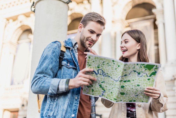 Low angle view of thoughtful boyfriend and happy girlfriend with map in city - Photo, Image