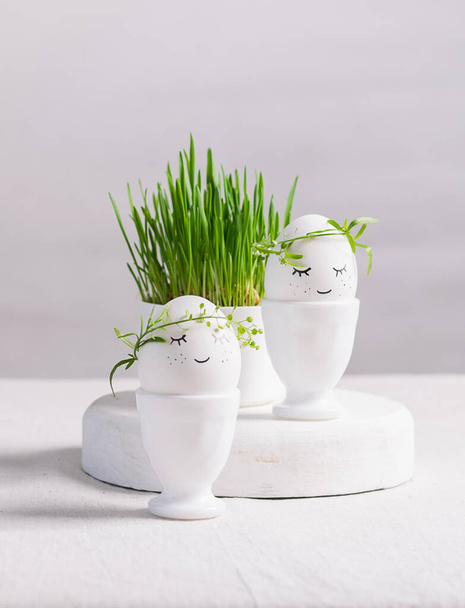 Ünnepi összetétel Húsvéti tojás csészékben és zöld növény csírák egy fehér asztalon. Fény háttér Boldog Húsvét koncepciót. - Fotó, kép