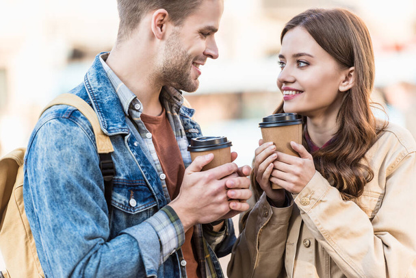 Man and girl holding disposable cups of coffee with clenched hands, looking at each other and smiling  - Foto, Imagem