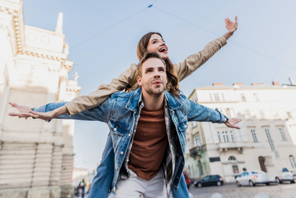 Low angle view of man with open arms piggybacking excited girl in city - Photo, Image