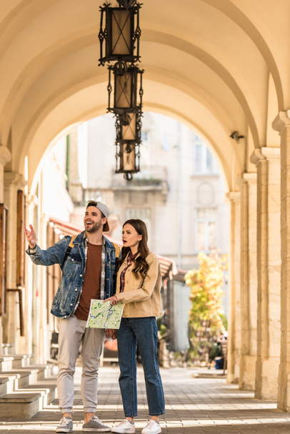 Selective focus of boyfriend pointing with hand and girlfriend with map excited and surprised in city - 写真・画像