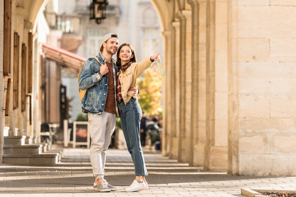 Selective focus of boyfriend hugging girlfriend pointing with finger and smiling in city - Фото, изображение