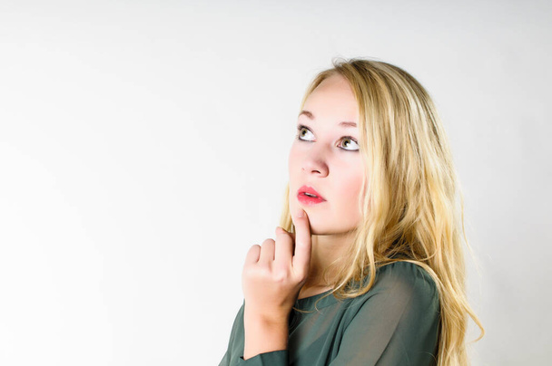 Attractive young woman with long blond hair has her fingers on her chin and looks thoughtfully into the air,isolated from a white background. - Fotoğraf, Görsel
