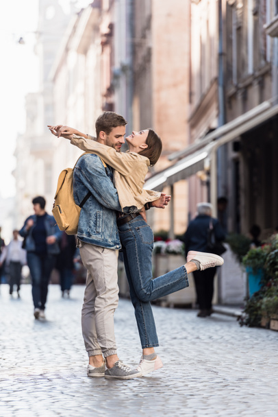 Boyfriend and girlfriend with raising leg hugging in city - Photo, image