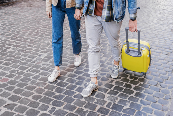 Cropped view of couple holding hands and traveling with suitcase together - Фото, зображення