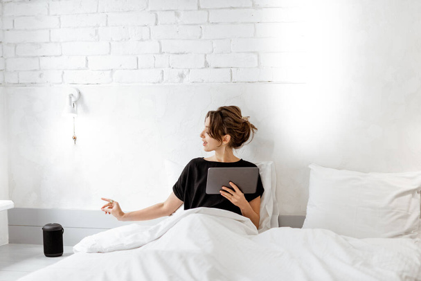 Femme relaxante avec un haut-parleur intelligent et une tablette dans la chambre
 - Photo, image