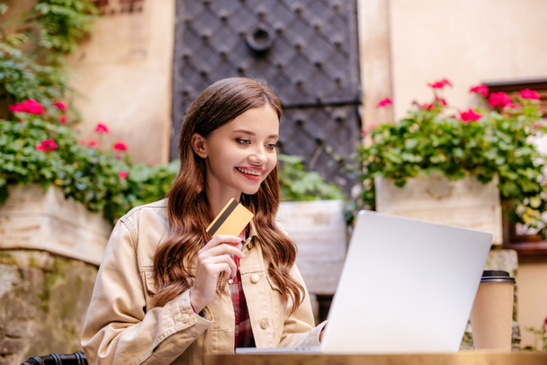 Selektiver Fokus einer lächelnden Frau mit Kreditkarte und Laptop in einem Café in der Stadt - Foto, Bild