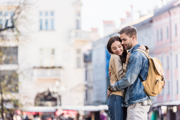 Freund und Freundin umarmen sich mit geschlossenen Augen und lächeln in der Stadt - Foto, Bild