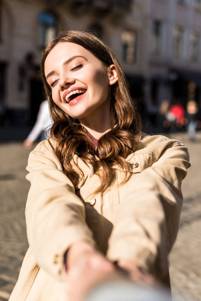 Cropped view of girl with closed eyes smiling and holding male hand in city - Фото, зображення