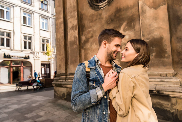 Man and woman holding hands, looking at each other and smiling near wall in city - Foto, Bild