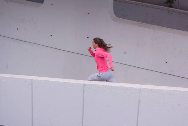 Молодая бегунья в толстовке на городской улице. Концепция городского спорта. Молодая женщина в спортивной одежде. - Фото, изображение