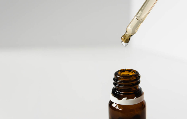 cosméticos, ácido hialurónico fluye de una pipeta en una botella de vidrio sobre un fondo blanco
 - Foto, Imagen