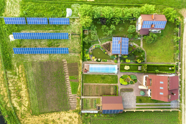 Vue aérienne d'une maison privée en été avec des panneaux photovoltaïques solaires bleus sur le toit et dans la cour. - Photo, image