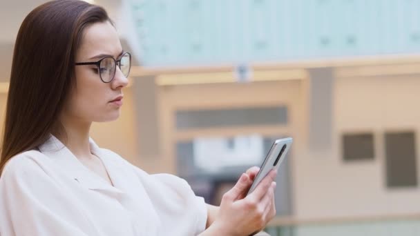 young woman in stylish business clothes and glasses uses a smartphone to communicate with a chatbot. - Felvétel, videó