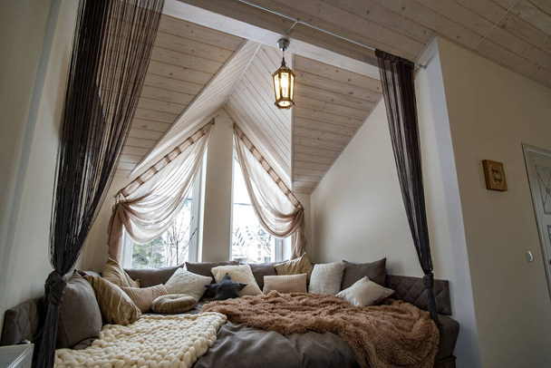 Modern bir evin içi geniş bir koridor ve büyük yumuşak bir dinlenme yeri. Çağdaş geniş kanepe, çok yastıklı ve pencereli ahşap tavan.. - Fotoğraf, Görsel