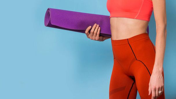 Sporty yoga girl with yoga mat wearing sportswear isolated over blue background, copy space - Фото, изображение