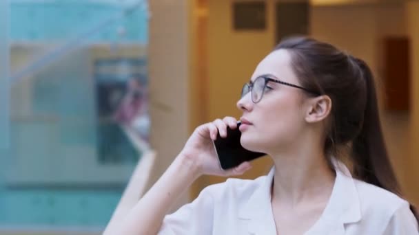 young business lady uses a smartphone. surprised girl in white shirt and glasses makes a phone call. - Imágenes, Vídeo