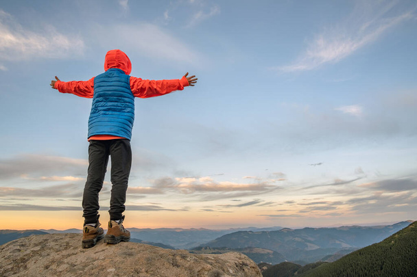 Young child boy hiker standing with raised hands in mountains enjoying view of amazing mountain landscape at sunset. - Photo, Image