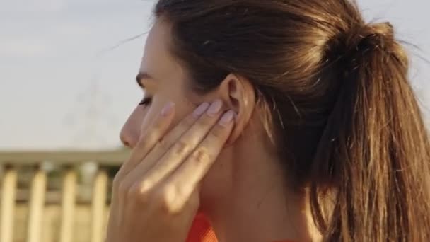 A calm young woman in an orange hoodie is turning on her earphones and starting to run outdoors on the bridge - Filmmaterial, Video