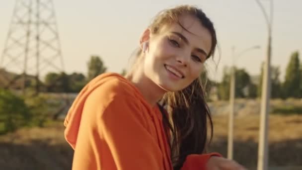 A smiling young woman in sportswear is standing near railing while turning to the sun on the bridge outdoors in the morning - Footage, Video