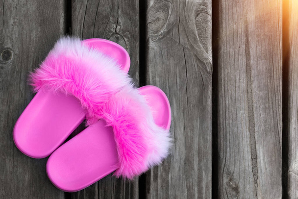 Close-up girl or woman empty glamour fashion fluffy fuzzy slippers standing on wooden floor board background. Toned flip-flop sliders near poolside. Vacation and travel concept. Copyspace. - Photo, Image