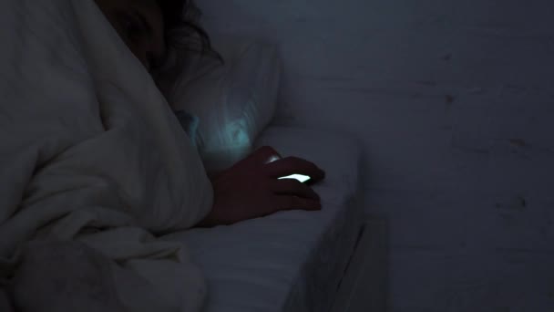 Joven en la cama por la noche utiliza un teléfono inteligente. Redes sociales y desplazamiento por Internet
, - Imágenes, Vídeo
