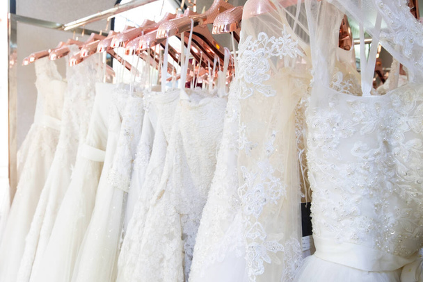 Beautiful, White bridal dress texture on background. Wedding dresses hanging on a hanger interior of bridal salon. Design, fashion modern luxury in detail. - Photo, image