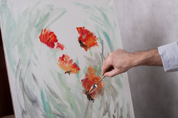 An artist with a palette knife paints red flowers on a white canvas. The beginning of a picturesque picture - 写真・画像