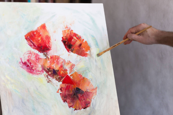 Artist's hand with a brush paints on a white canvas. The beginning of a picturesque picture - 写真・画像