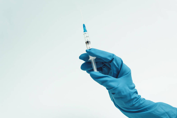 La main du médecin dans un gant de caoutchouc bleu tient une seringue médicale sur un fond bleu. Le concept de médecine et de soins médicaux pour le patient
. - Photo, image