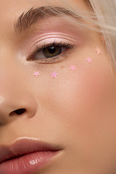 Half close-up portrait of a woman with shiny clean skin and curly blond hair. Rhinestones stars on the eyes, nude makeup and natural lipstick. soft care, full lips, long eyelashes and thick eyebrows - Foto, afbeelding