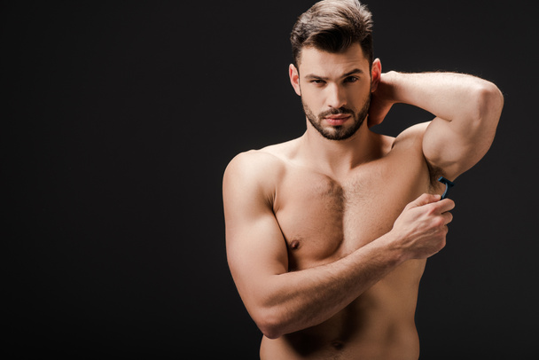 handsome naked man shaving armpits with razor isolated on black - Photo, Image