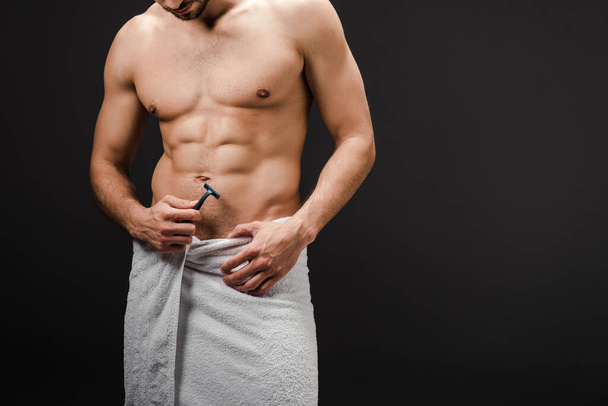 cropped view of muscular shirtless man in towel holding razor isolated on black - Φωτογραφία, εικόνα