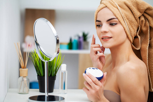 Cute girl puts on face cream in the bathroom - Photo, Image