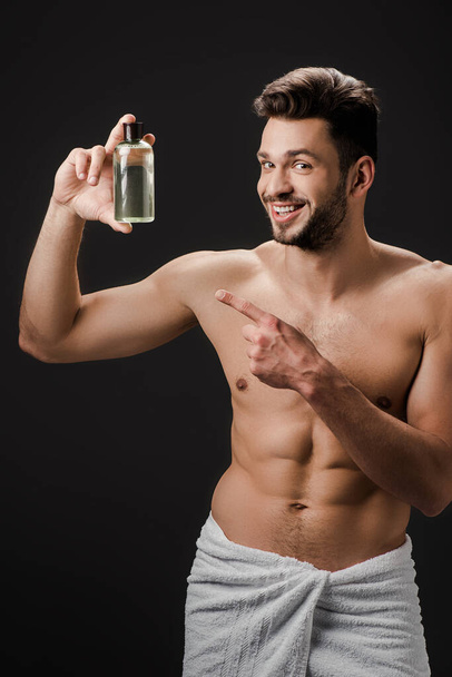 sexy alegre homem apontando para garrafa de colônia isolado no preto
 - Foto, Imagem