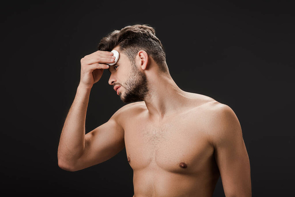 σέξι γυμνός άντρας που χρησιμοποιεί μαξιλάρι καλλυντικού βαμβακιού απομονωμένο σε μαύρο - Φωτογραφία, εικόνα
