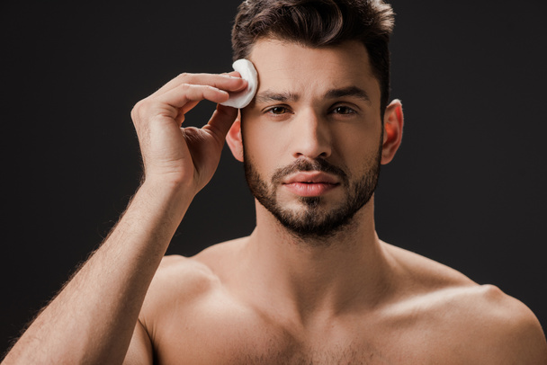 handsome nude man using cosmetic cotton pad isolated on black - Φωτογραφία, εικόνα