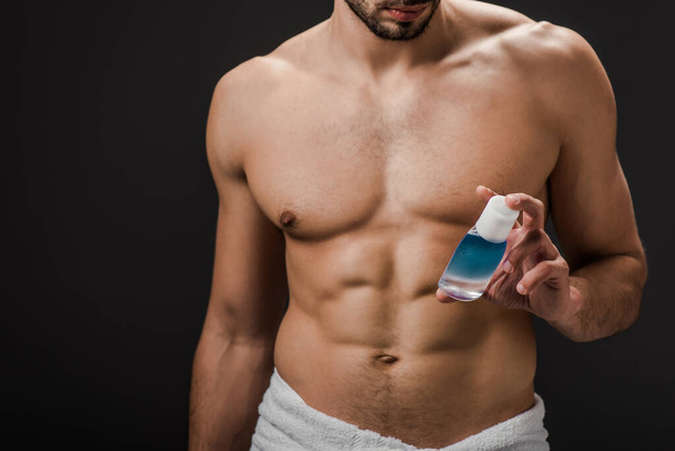 oříznutý pohled na sexy bez trička muž drží láhev s kosmetickou kapalinou izolované na černé - Fotografie, Obrázek