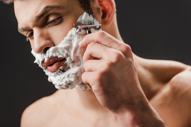 schöner verführerischer Mann rasiert Gesicht mit Rasiermesser isoliert auf grau - Foto, Bild