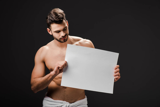 sexy shirtless man in towel holding blank placard isolated on black - 写真・画像
