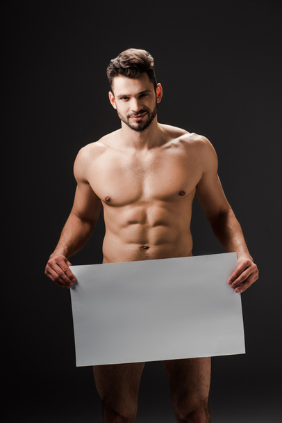happy sexy naked man holding blank placard isolated on black - 写真・画像