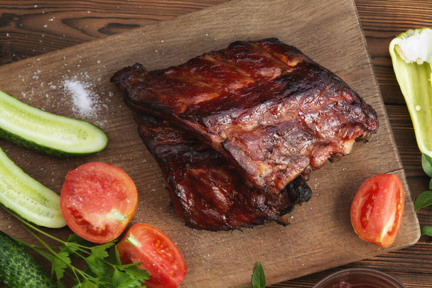 Barbecue pork ribs on a wooden cutting board with ketchup and vegetables - Valokuva, kuva