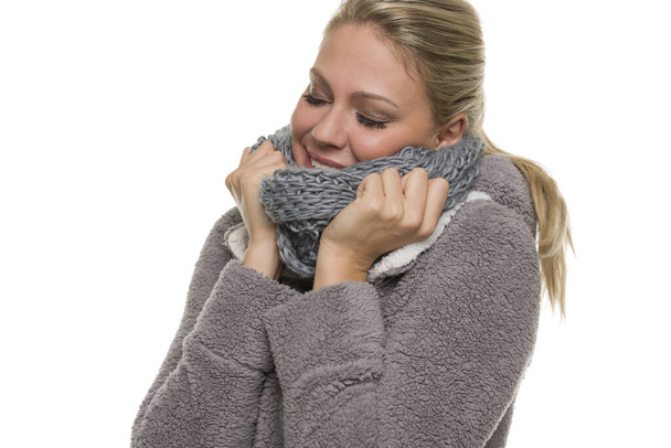 The face and hands of a blonde woman cuddle and bury themselves in a knitted scarf. - Foto, afbeelding
