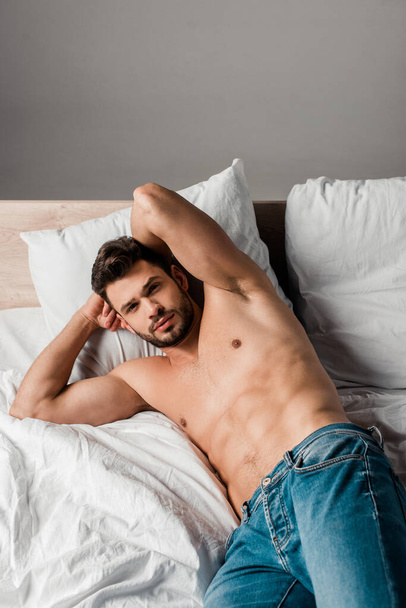 sexy shirtless man in jeans lying on bed on grey - Фото, зображення