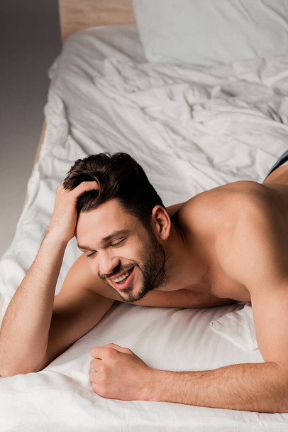 sexy smiling man in jeans lying on bed on grey - Photo, image