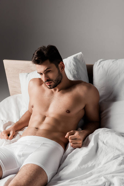 bearded handsome sexy man lying on bed on grey - Фото, изображение