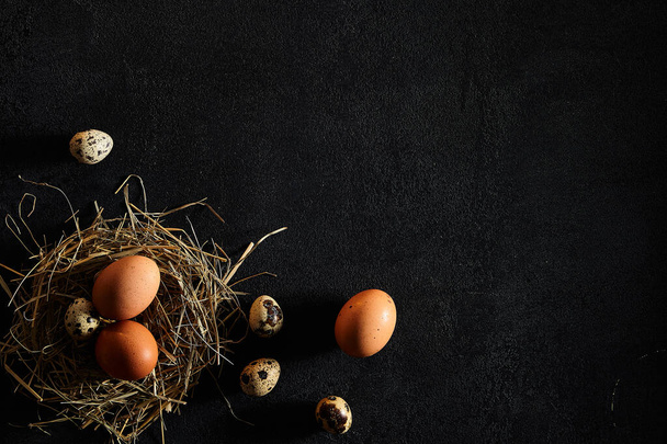 Kwartels en kippeneieren in abstracte nest op rustieke zwarte achtergrond. Pasen, lente of eco food concept. Top View, kopieer ruimte - Foto, afbeelding