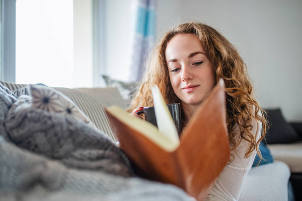 Young woman relaxing indoors at home with book. - 写真・画像