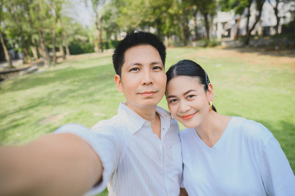 Lähikuva laukaus Happy hymyilevä aasialainen pari ottaa selfie ulkona. Mies ottaa kuvan vaimonsa kanssa puistossa.
 - Valokuva, kuva